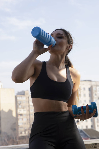 Blonde fit woman in black sportswear standing and posing with bottle of water . High quality photo - Fotó, kép