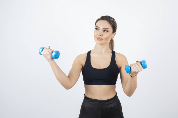 Blonde fit woman in black top standing and exercising with dumbbells . High quality photo - Zdjęcie, obraz