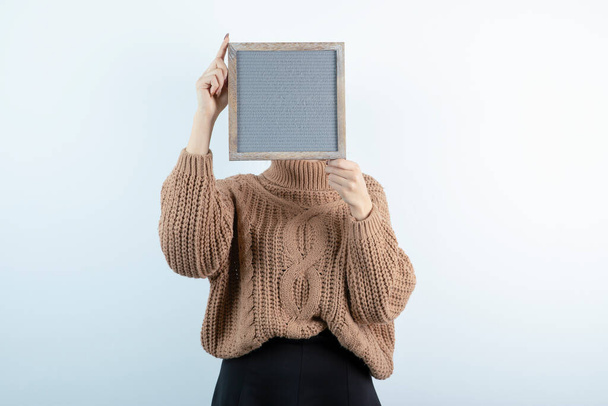 Portrait of beautiful woman in knitwear hiding behind empty frame. High quality photo - Photo, Image