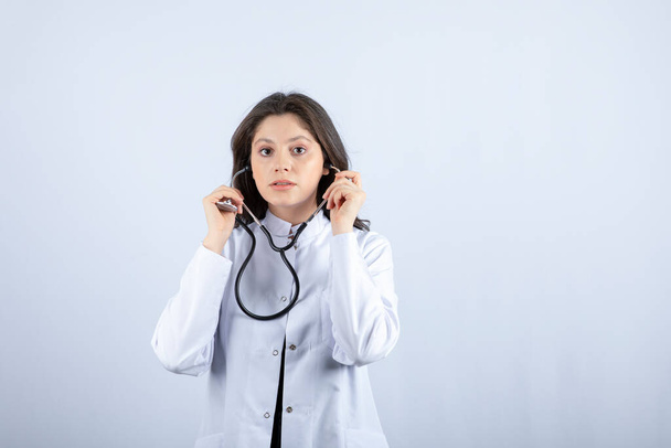 Młoda lekarka używająca stetoskopu do sprawdzania pulsu na białym tle. Wysokiej jakości zdjęcie - Zdjęcie, obraz