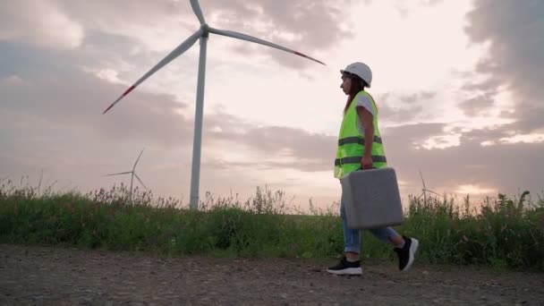 Специалист по экологии женщина со специальным оборудованием в руке идет на обслуживание ветряной мельницы - Кадры, видео