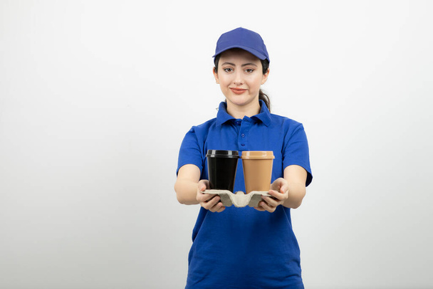 Mulher bonita de uniforme azul mostrando copos em uma caixa para câmera. Foto de alta qualidade - Foto, Imagem