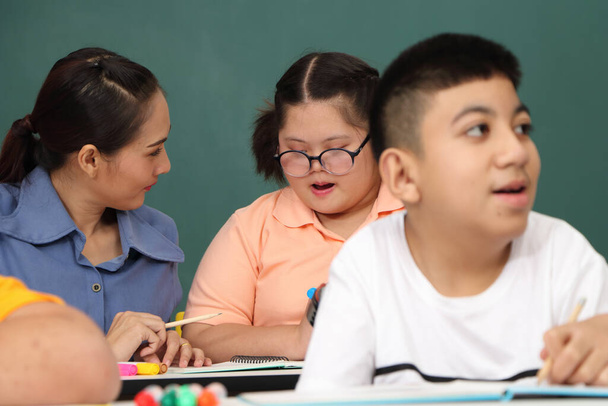 Asiatische behinderte Kinder Oder ein autistisches Kind lernt lesen, schreiben und trainiert seine Hand- und Fingermuskeln mit einem Lehrer am Schultisch. Konzentrieren und lächeln Glückliches Behindertenkonzept - Foto, Bild