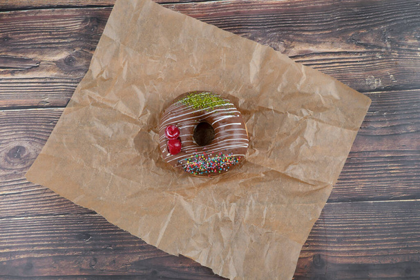 Γλυκό κομμάτι ντόνατ σοκολάτας με επικάλυψη σοκολάτας τοποθετείται σε λαδόκολλα. Υψηλής ποιότητας φωτογραφία - Φωτογραφία, εικόνα