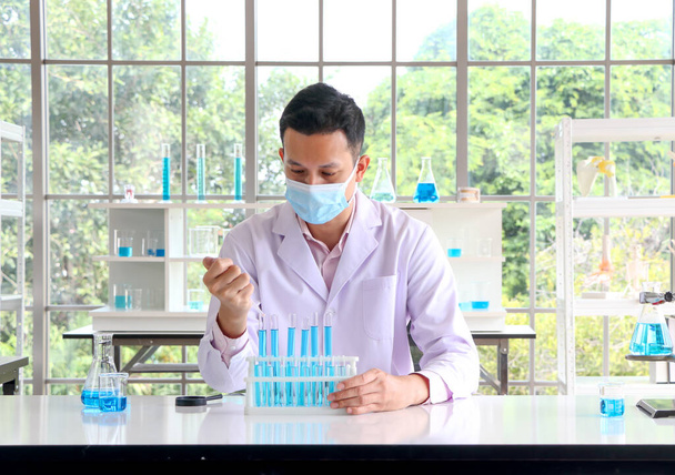 Un científico o químico asiático deja caer un líquido químico azul en un laboratorio. Conceptos de investigación en salud, farmacia y medicina. Análisis de líquidos para separar ADN y moléculas in vitro. - Foto, imagen