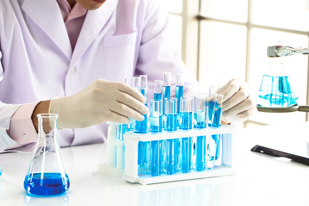 Egy ázsiai tudós vagy vegyész egy kék folyékony vegyszert dob egy laboratóriumba. Kutatás fogalmak egészségügyi, gyógyszertár, és az orvostudomány. Folyadékanalízis a DNS és molekulák in vitro elkülönítésére. - Fotó, kép