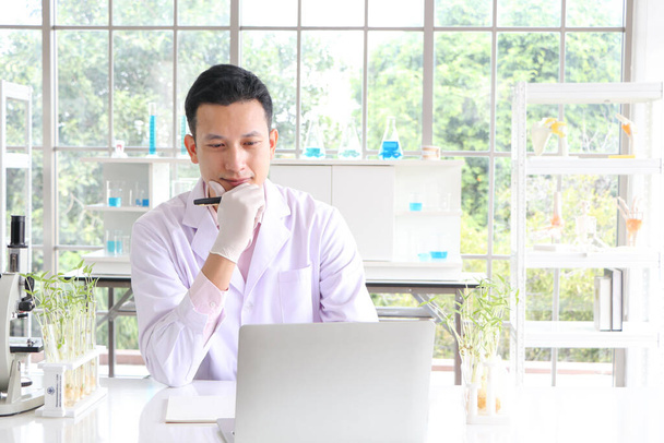 Азиатские исследователи в белых халатах Концепция работы в научной лаборатории с помощью ноутбука, чтобы найти информацию и записать в книгу результатов испытаний или сделать доклад в научной лаборатории - Фото, изображение