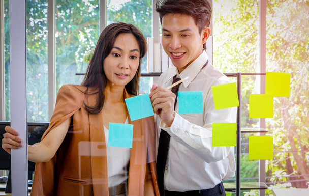 Hommes et femmes d'affaires asiatiques regardant et écrivant des notes post-it pour le remue-méninges. Mettez un message sur le miroir dans le bureau Plan de travail, remue-méninges, stratégie Mode de vie créatif, Succès dans le concept d'entreprise - Photo, image