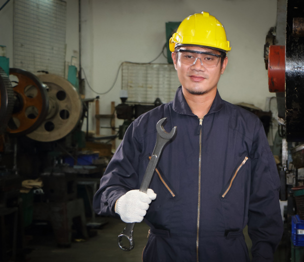 Азіатський робітник В галузях, які носять окуляри, захисні капелюхи і форму безпеки Власник знарядь стоїть технічного обслуговування в промисловості з довірою - Фото, зображення