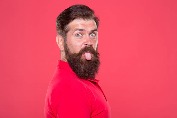 Bearded and playful. Bearded man stick tongue out red background. Unshaven hipster with bearded face. Barbershop. Beard grooming. Skincare. Haircare. Mens cosmetics. Bearded and brutal, copy space - Foto, immagini