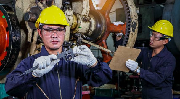 Два азіатських чоловіки-працівники в захисному одязі використовують Vernier calipers. Перевірте якість і вимірюйте запасні частини робочих машин на промислових заводах і виробничих процесах.. - Фото, зображення