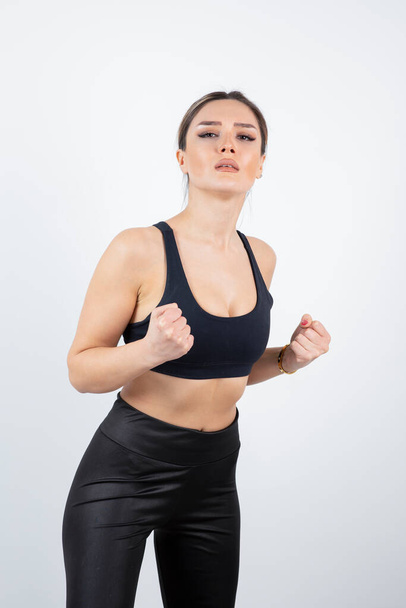 Blonde fit woman in black sportswear standing and posing over a white wall . High quality photo - Photo, Image
