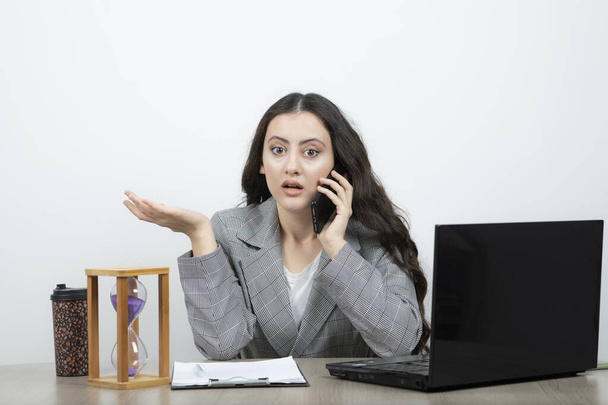 Jeune femme d'affaires assise au bureau avec ordinateur portable et sablier appelant. Photo de haute qualité - Photo, image
