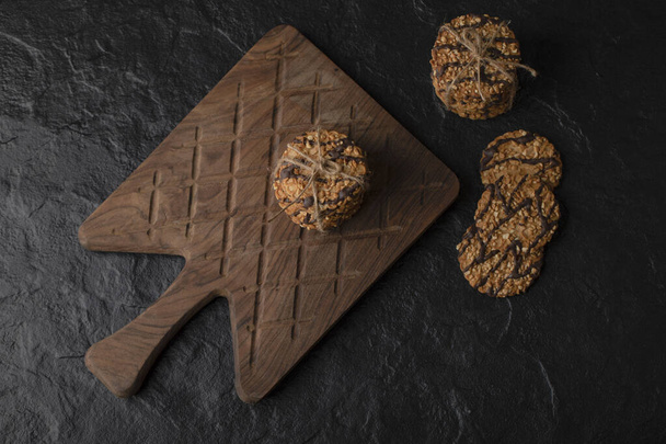 Domácí sezamové sušenky na dřevěné řezací desce nad černým pozadím. Kvalitní fotografie - Fotografie, Obrázek