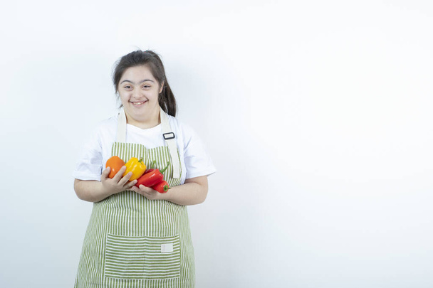 Young pretty girl standing in checkered apron and holding vegetables . High quality photo - Photo, Image