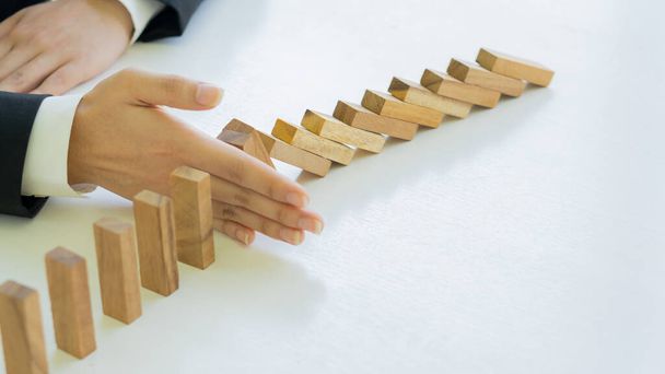 A businessman's hand stops a wooden block domino from falling continuously or a successful intervention strategy. and ideas for close-up business on the table - Zdjęcie, obraz