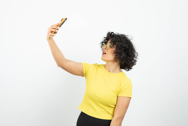 mladá žena s chytrým telefonem pózování na bílém pozadí  - Fotografie, Obrázek