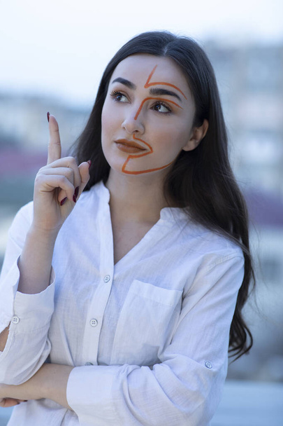  Egy festett arcú, ujjal mutogató fiatal nő portréja. Kiváló minőségű fénykép - Fotó, kép
