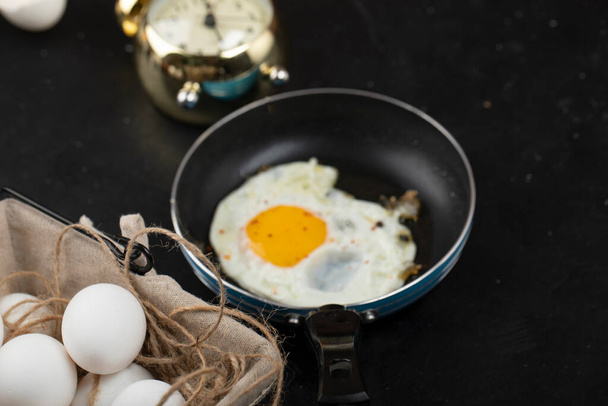 Herkullinen aamiainen aurinkoisella puolella paistettuja munia paistinpannulla ja herätyskellolla. Laadukas kuva - Valokuva, kuva