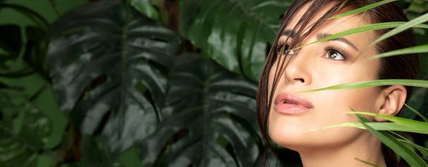 Красивая натуральная молодая женщина с безупречной кожей среди зеленых тропических листьев в концепции оздоровления, природной красоты и ухода за кожей или спа-процедуры - Фото, изображение