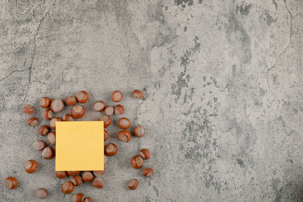 Terveet macadamiapähkinät keltaisella neliötarralla kivipohjalla. Laadukas kuva - Valokuva, kuva