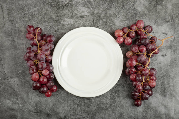 White plate and red delicious grapes on marble table. High quality photo - Φωτογραφία, εικόνα