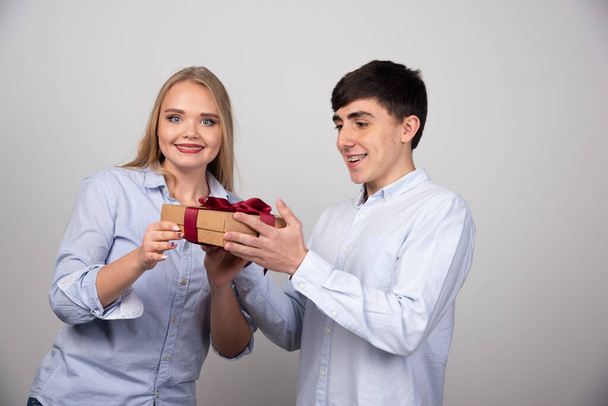 Hermosa chica dando a su novio un regalo sobre fondo gris. Foto de alta calidad - Foto, Imagen
