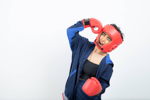 Foto van een fitte vrouwelijke bokser in rode handschoenen en een helm die zichzelf stompt. Hoge kwaliteit foto - Foto, afbeelding