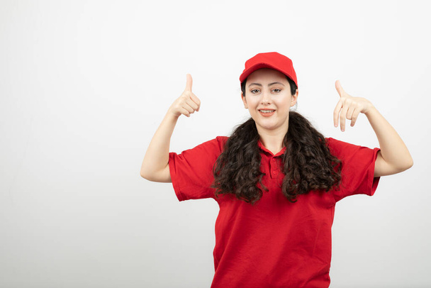 親指を示す赤い制服を着た笑顔の女性の肖像。 - 写真・画像