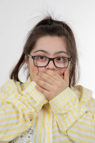 Foto eines jungen Mädchens mit Down-Syndrom, das steht und Mund mit Händen bedeckt. Hochwertiges Foto - Foto, Bild