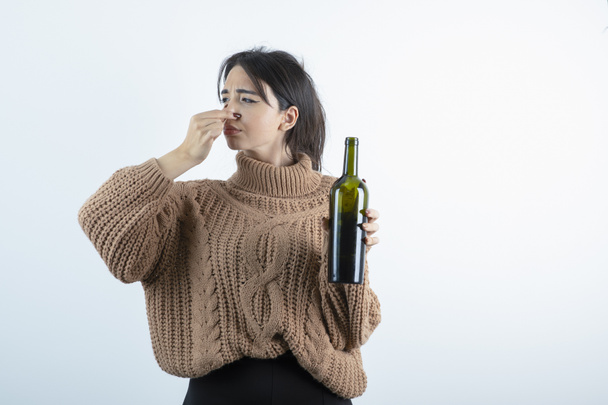 Portrait of young woman with bottle of wine holding her nose because of smell. High quality photo - Фото, зображення
