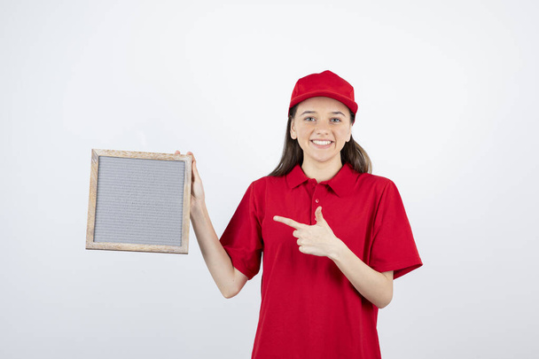 Bild eines jungen Teenie-Mädchens in roter Uniform, das auf den Rahmen zeigt. Hochwertiges Foto - Foto, Bild