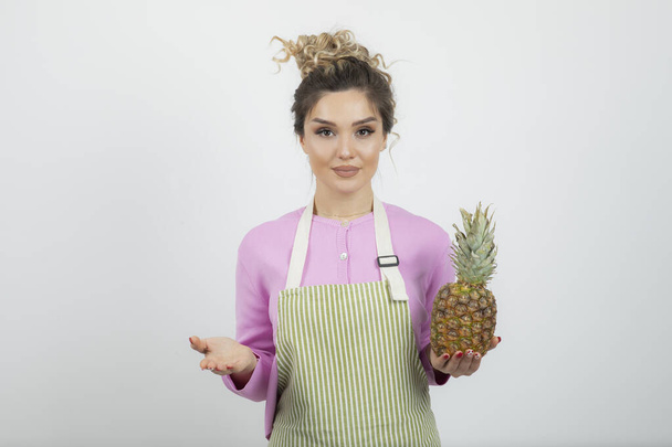 Portrait of beautiful woman in apron holding ripe pineapple. High quality photo - Photo, Image