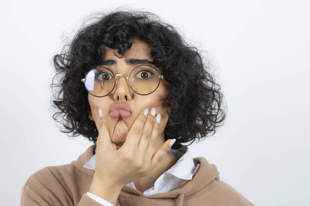 Capelli ricci donna bruna in occhiali rendendo faccia divertente su bianco. Foto di alta qualità - Foto, immagini