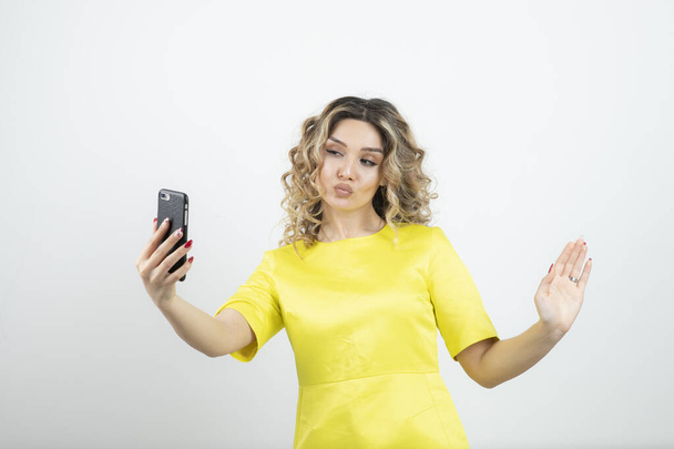 Bild eines hübschen Mädchens in gelbem Kleid mit welligem Haar, das ein Selfie macht. Hochwertiges Foto - Foto, Bild