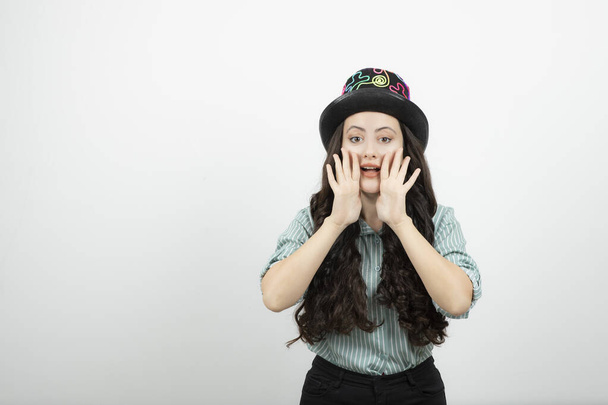 Mladá žena s dlouhými vlasy v kouzelnickém klobouku, držící se za ruce u úst. Kvalitní fotografie - Fotografie, Obrázek
