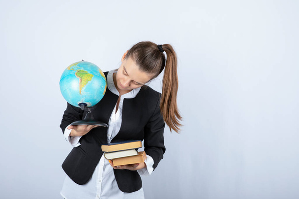 Foto des jungen Lehrers, der Bücher und Globus auf weißem Hintergrund betrachtet. Hochwertiges Foto - Foto, Bild
