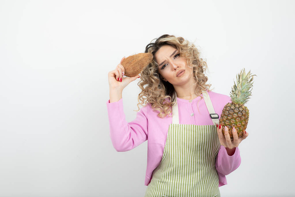 Красивая кудрявая женщина в фартуке держит тропические фрукты над белым. Высокое качество фото - Фото, изображение