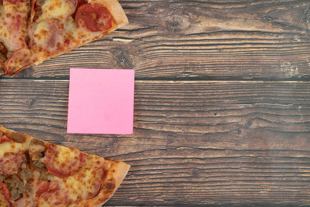 Sabrosa pizza de pepperoni y almohadilla rosa memo en la mesa de madera. Foto de alta calidad - Foto, Imagen