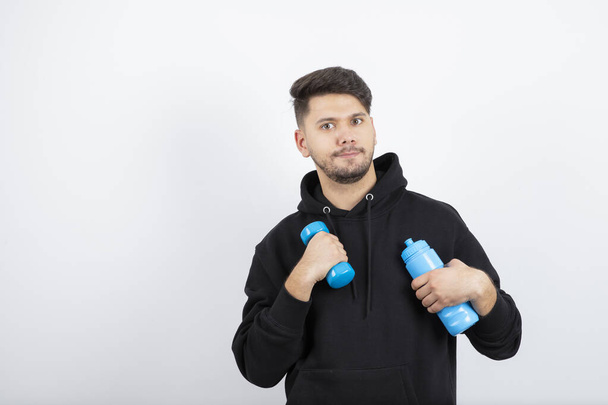 Portrait of young handsome guy holding blue dumbbell and water bottle. High quality photo - Foto, Bild