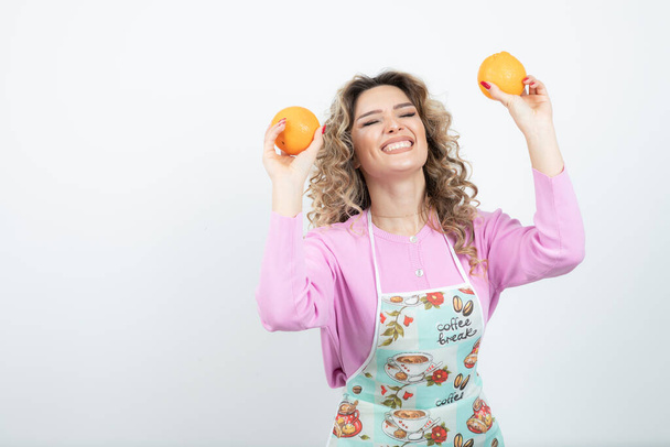 Portrait of young curly woman in apron posing with oranges. High quality photo - Fotografie, Obrázek