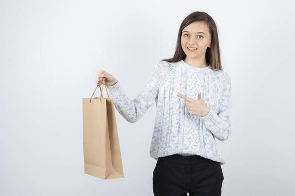 Photo d'une adolescente en pull pointant vers un sac artisanal. Photo de haute qualité - Photo, image