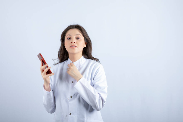 Photo of young doctor holding cellphone on white background. High quality photo - Foto, Imagen
