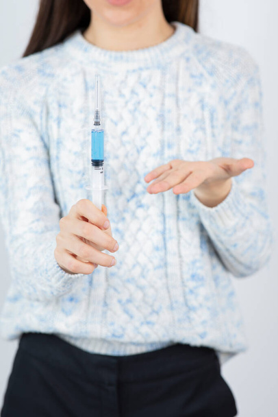 Ženské ruce drží injekční stříkačku na nemoc přes bílou stěnu. Kvalitní fotografie - Fotografie, Obrázek