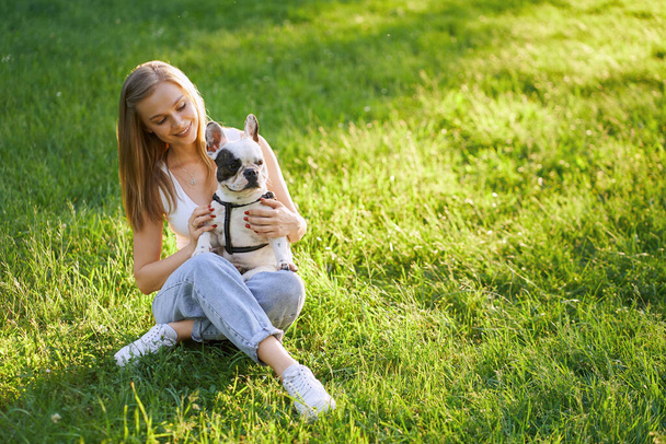 Smiling woman hugging french bulldog on grass. - Foto, afbeelding