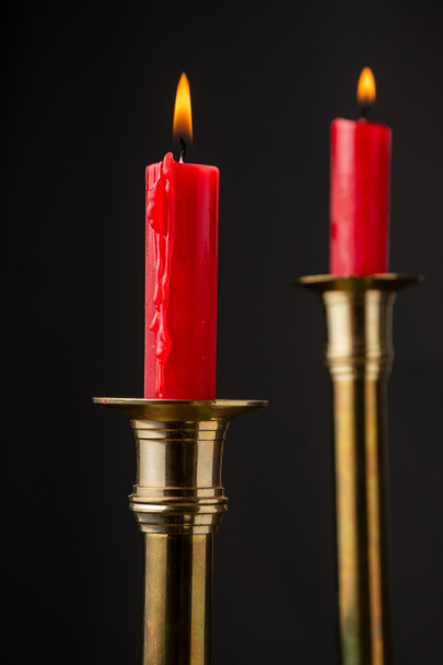 Close-up of two burning red candles in golden candlestick, with selective focus, black background, vertical - Photo, Image