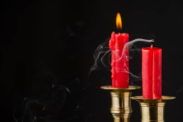 Detailní záběr dvou červených svíček, jedna nerozsvícená a jedna rozsvícená, ve zlatém svícnu, selektivní zaostření, černé pozadí, horizontální, s kopírovacím prostorem - Fotografie, Obrázek