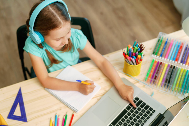 attentive little girl wearing headphones uses laptop to make video call with her teacher. child is happy to learn remotely. schoolgirl is happy to receive knowledge. E-Education Distance Home Learning - Fotoğraf, Görsel