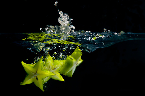A trio of star fruit pieces create a splash as they hit the water - Φωτογραφία, εικόνα