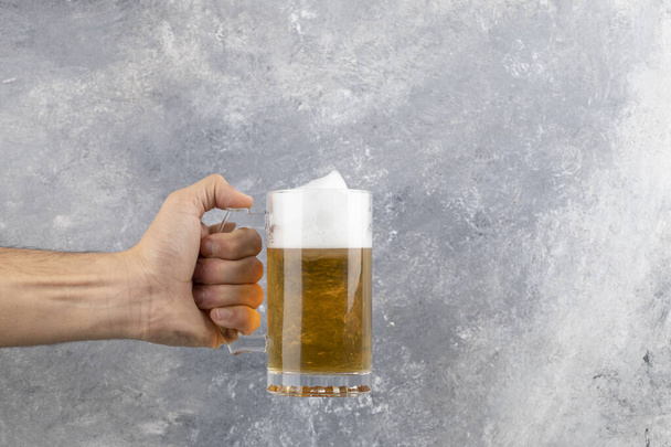 Mannelijke hand met een mok koud schuimig bier op marmeren achtergrond. Hoge kwaliteit foto - Foto, afbeelding